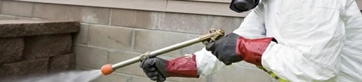 Pest control technician applying exterior insect treatment along a home foundation in Pittsburgh, PA