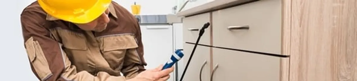 Roach exterminator applying treatment under kitchen cabinets in Pittsburgh, PA