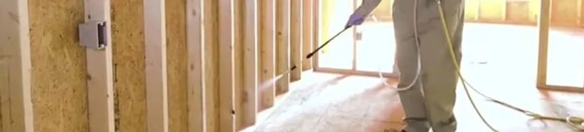 Termite treatment technician applying spray along framing and unfinished walls in Pittsburgh, PA